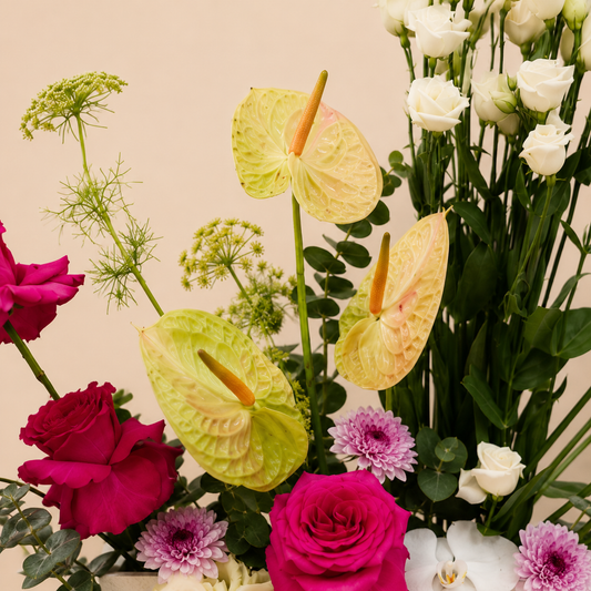 A close-up floral arrangement featuring pale yellow and lime green anthuriums, deep pink and white roses, purple chrysanthemums, white orchids, and green foliage, online flowers delivery UAE.