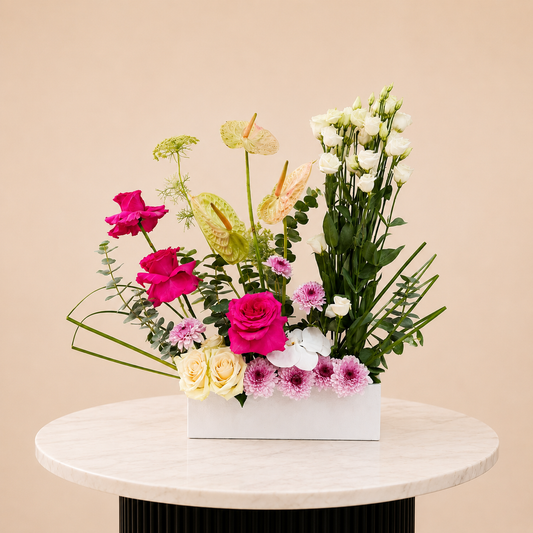 A rectangular white flower box filled with a mixed floral arrangement featuring bright pink roses, white roses, pale yellow roses, green anthuriums, and pink chrysanthemums, online flowers arrangement delivery Dubai.