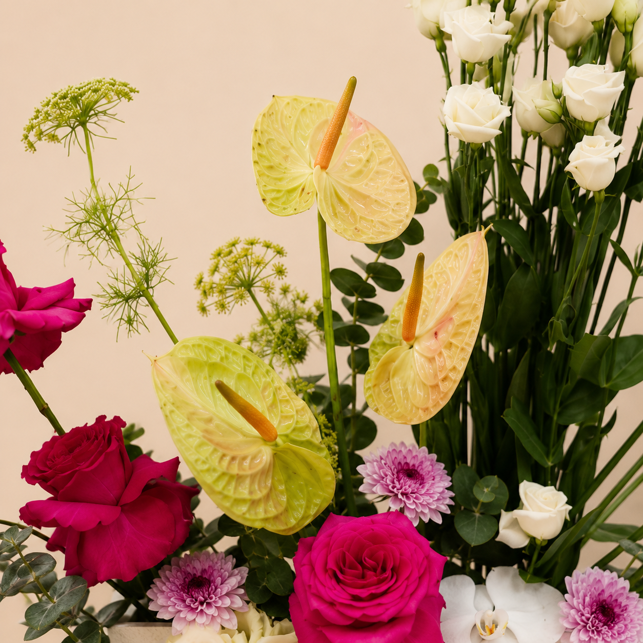 A close-up floral arrangement featuring pale yellow and lime green anthuriums, deep pink and white roses, purple chrysanthemums, white orchids, and green foliage, online flowers delivery UAE.