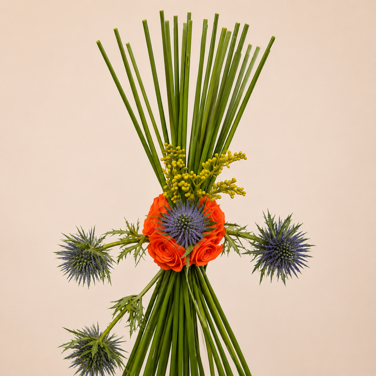 Elegant contemporary floral arrangement with peach and orange roses, blue eryngium, steel grass, and greenery in a modern black vase. online flowers delivery Dubai.