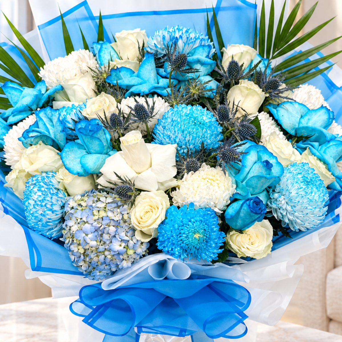 A vibrant blue and white flower bouquet featuring roses, chrysanthemums, hydrangeas, and blue lotus flowers, wrapped in blue and white paper with a blue ribbon bow.