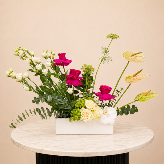 A rectangular white flower box filled with an arrangement of white roses, magenta roses, white snapdragons, green eucalyptus, and pale yellow anthuriums, arrangement fresh flowers delivery Dubai.