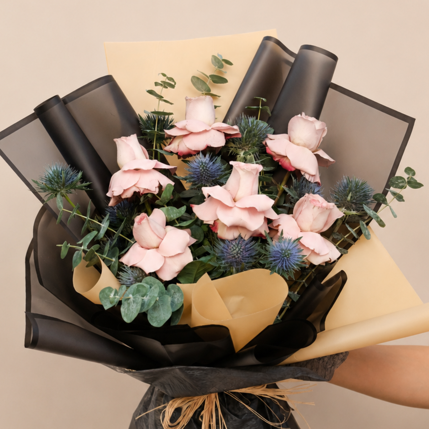 A bouquet of pink roses, blue thistle flowers, and green eucalyptus stems wrapped in black and beige paper, delivery Dubai