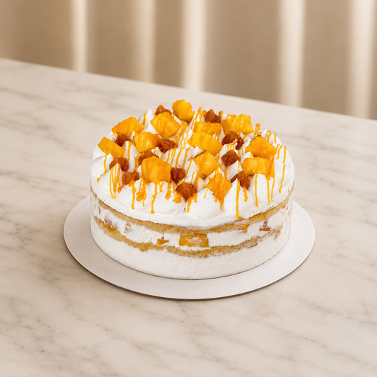 A semi-naked cake with white frosting, topped with diced mango pieces, caramel drizzle. delivery all over UAE