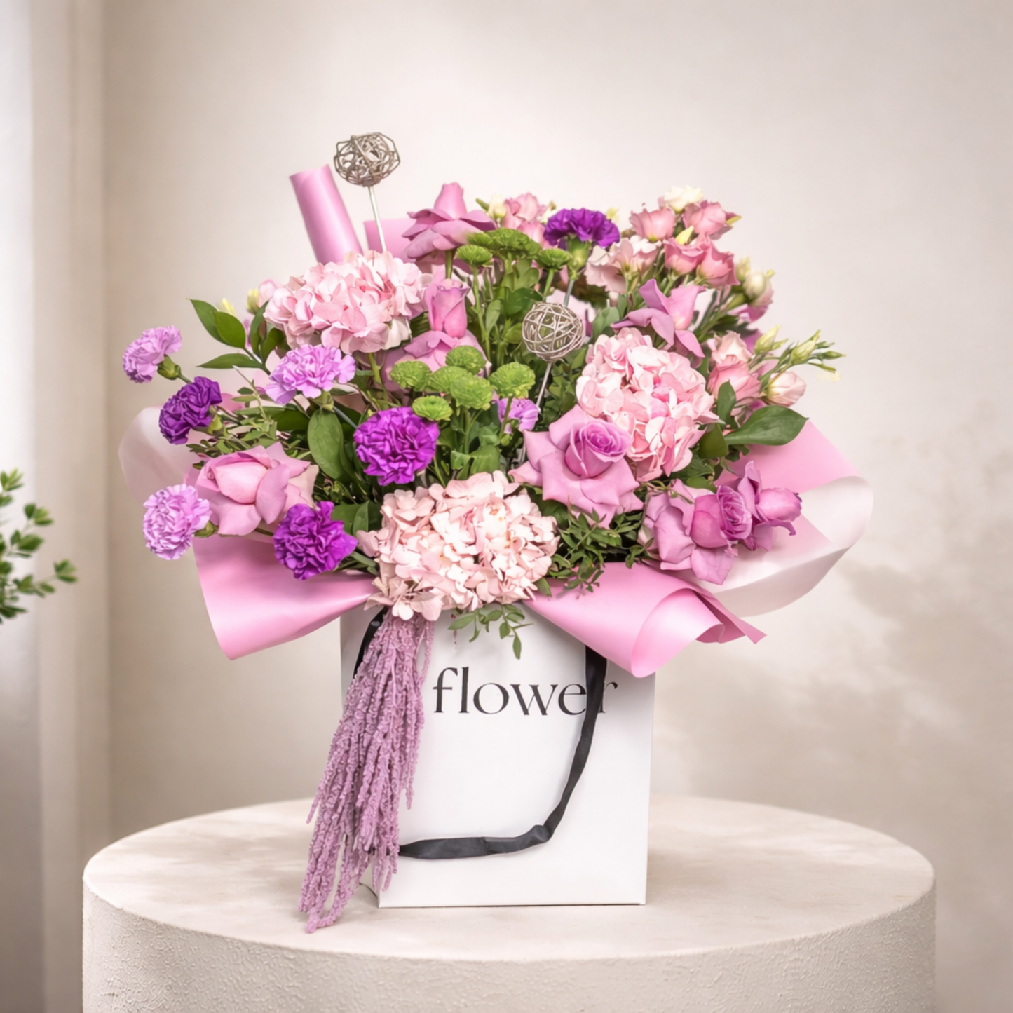 Pink and purple mixed flower arrangement in a white luxury bag with ribbon and lush greenery.